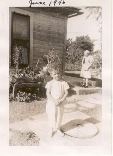 Four year old Kirk poses near the farm house where he was born as was his father.  Grandmother Wood is on the porch step.